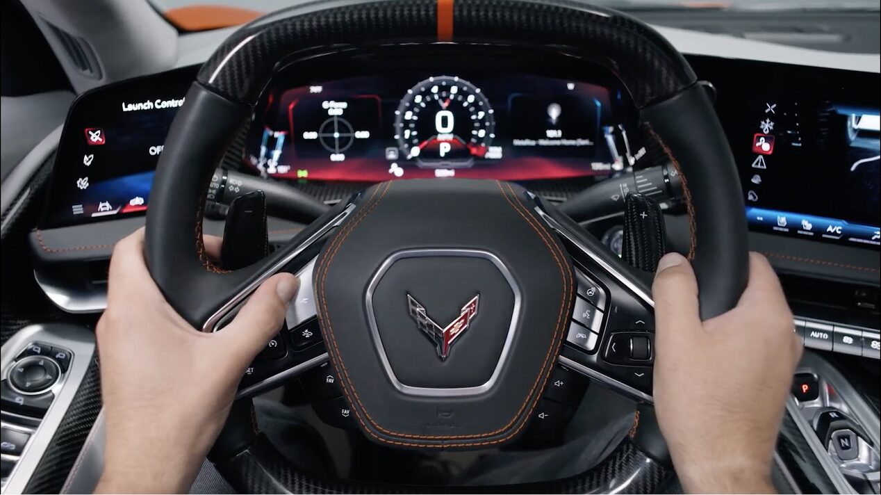 A Driver Holding the Steering Wheel of a Chevy Corvette with the Digital Instrument Cluster Displaying Performance Gauges.