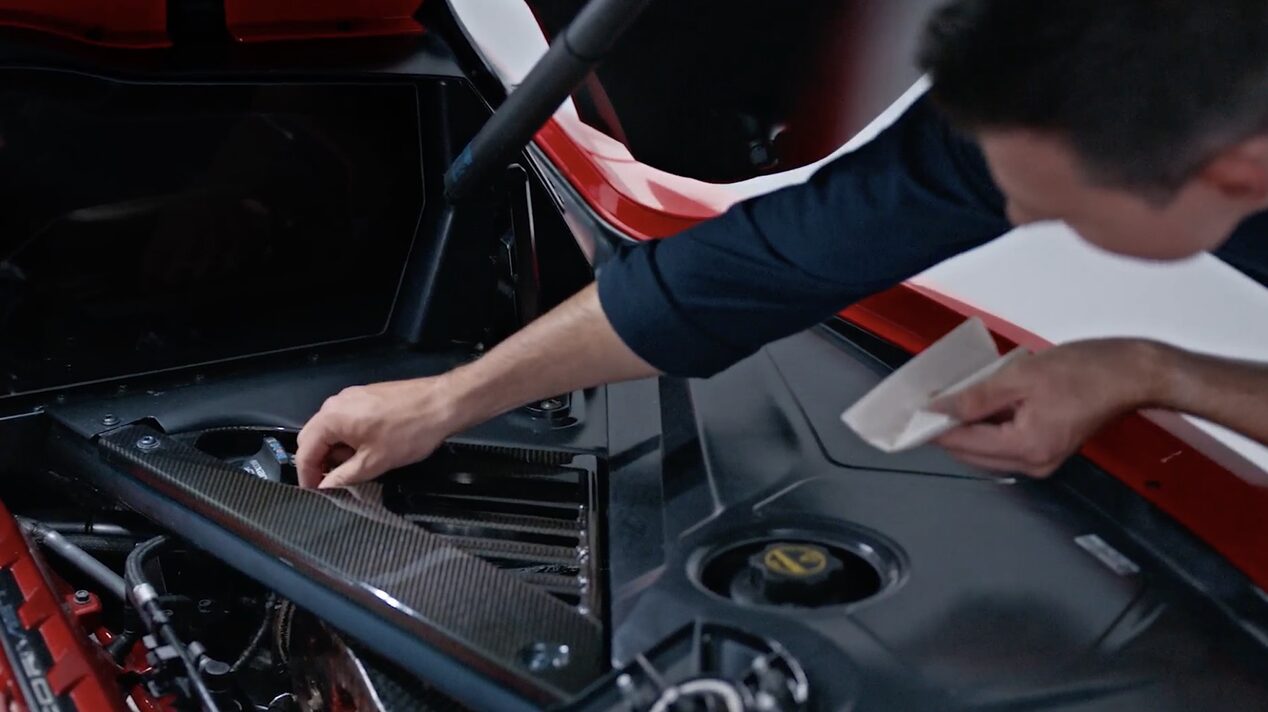 A Person Inspecting the Rear Engine Compartment of a Red Chevy Corvette with the Hood Open.
