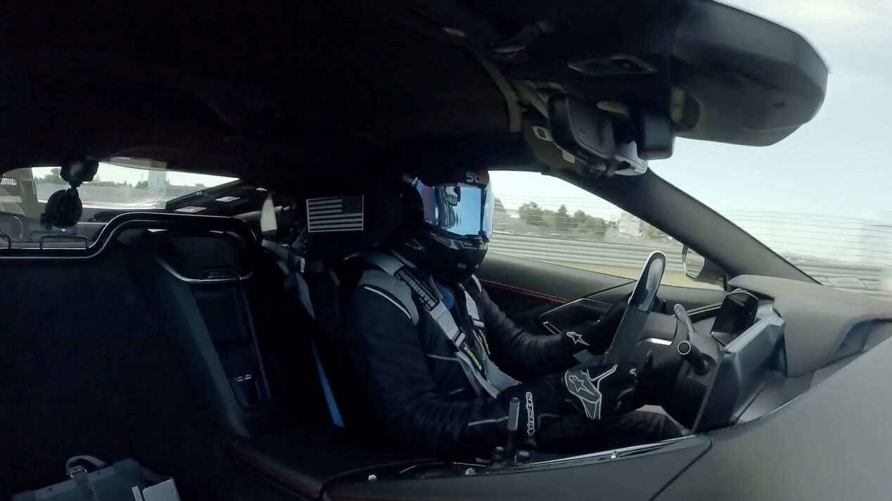 A Race Car Driver Wearing a Helmet and Gloves Driving a Chevy Corvette on a Track.