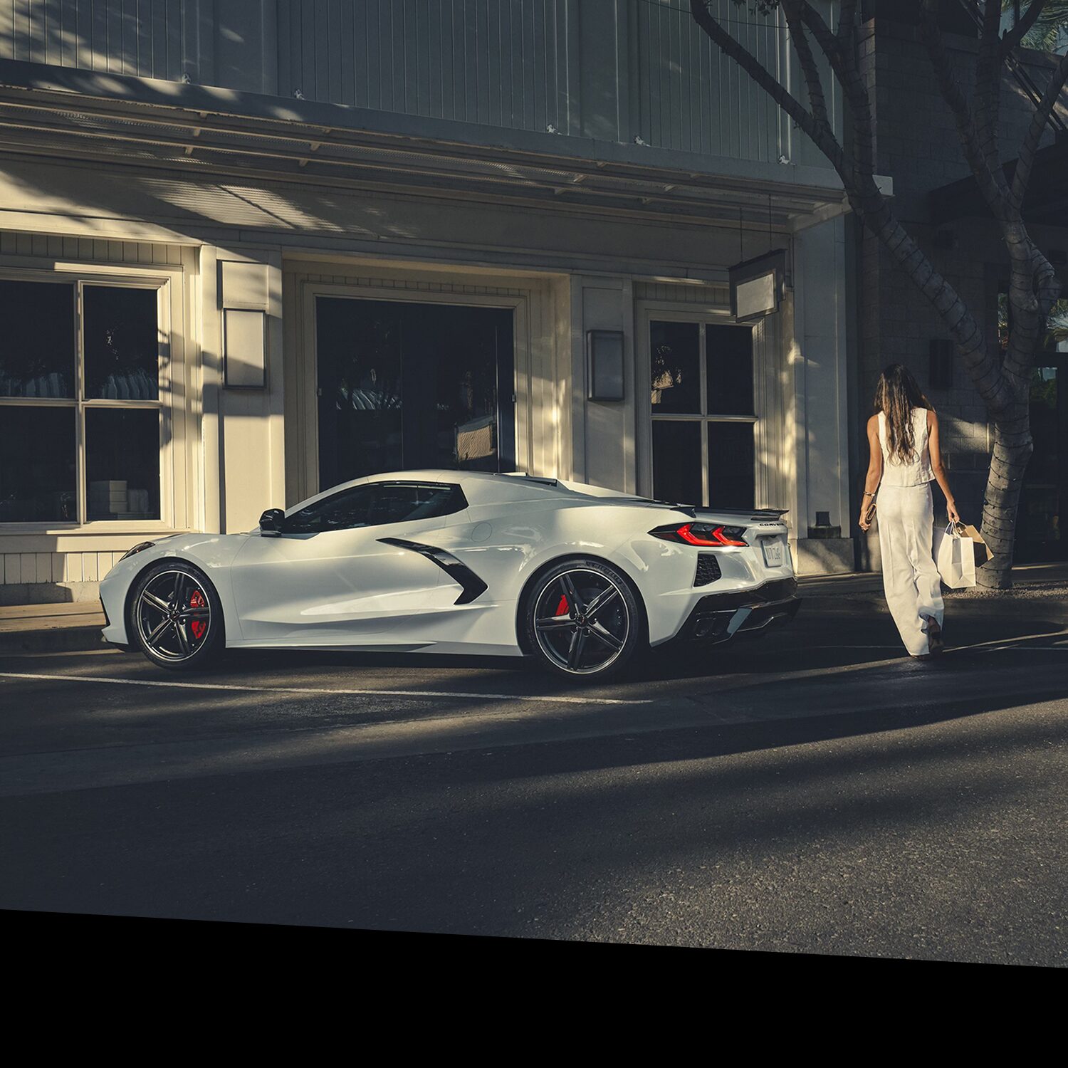 A White Chevrolet Corvette Parked on a Sunlit Street in Front of a Building with Large Windows and Decorative Columns.