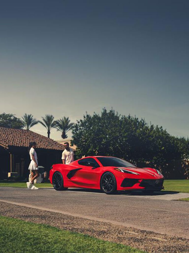 A Red Chevy Corvette in a Parking Spot with a Man and Woman Walking Towards the Car