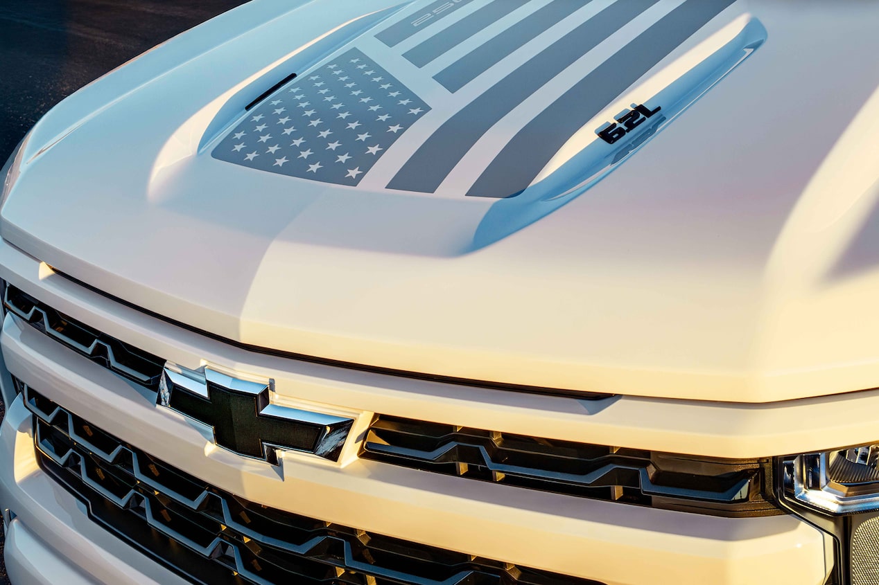 Front Angled View of a White Chevy Truck with a Gray Design of the American Flag on the Hood.
