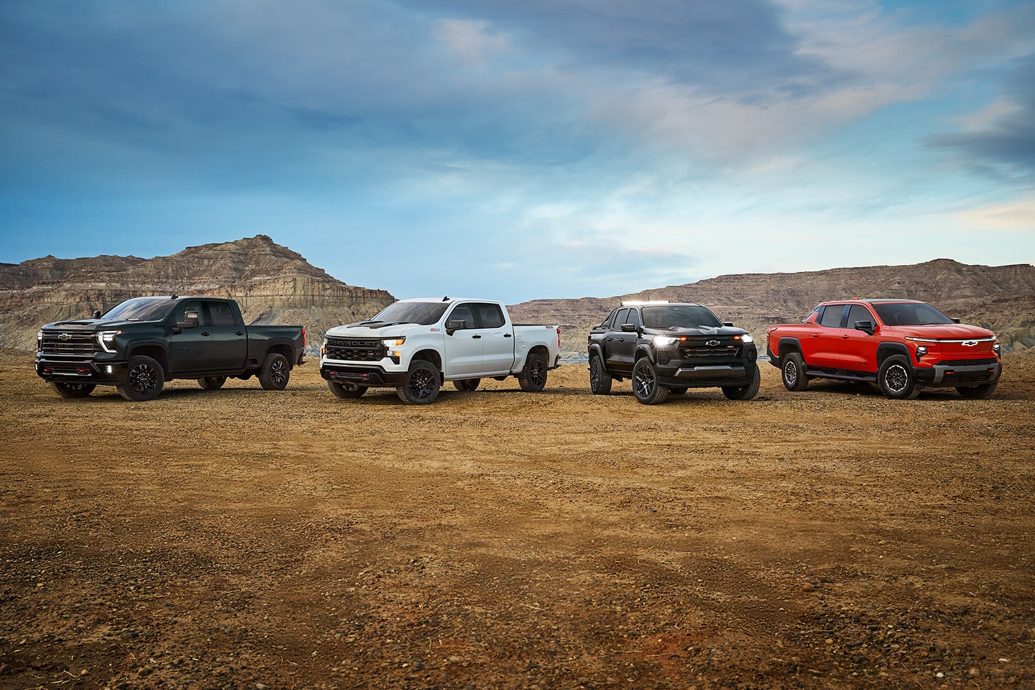 Chevy Truck Line-up on a Dirt Path with Mountains in the Background.