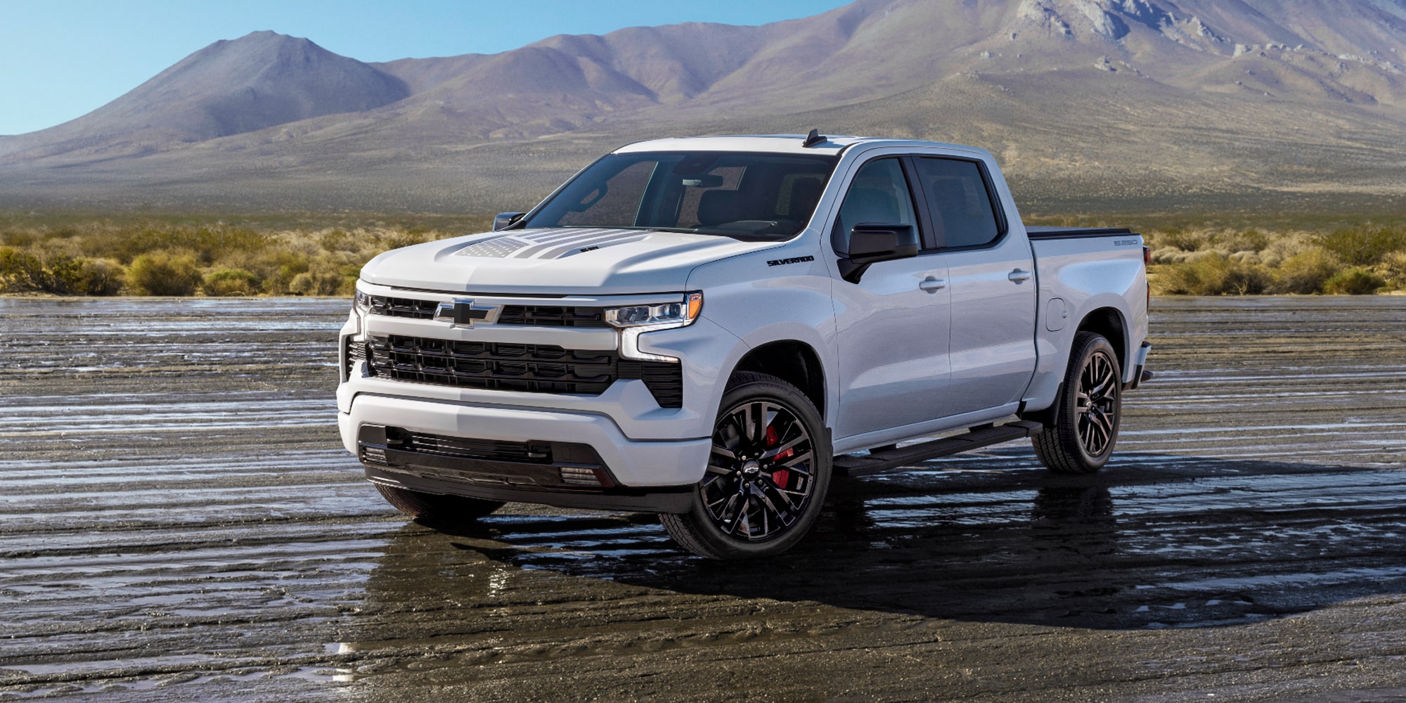 A White Chevy 4-Door Truck Parked on a Muddy Field with Mountains in the Background.