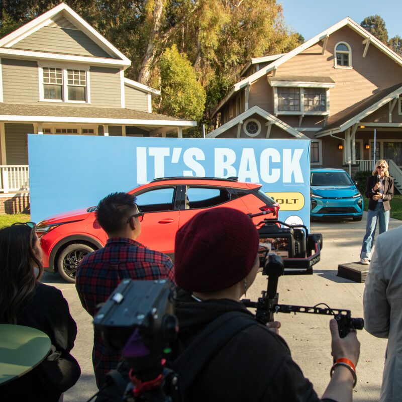 2027 Chevrolet Bolt in Habanero Orange Parked in Front of a Group of People