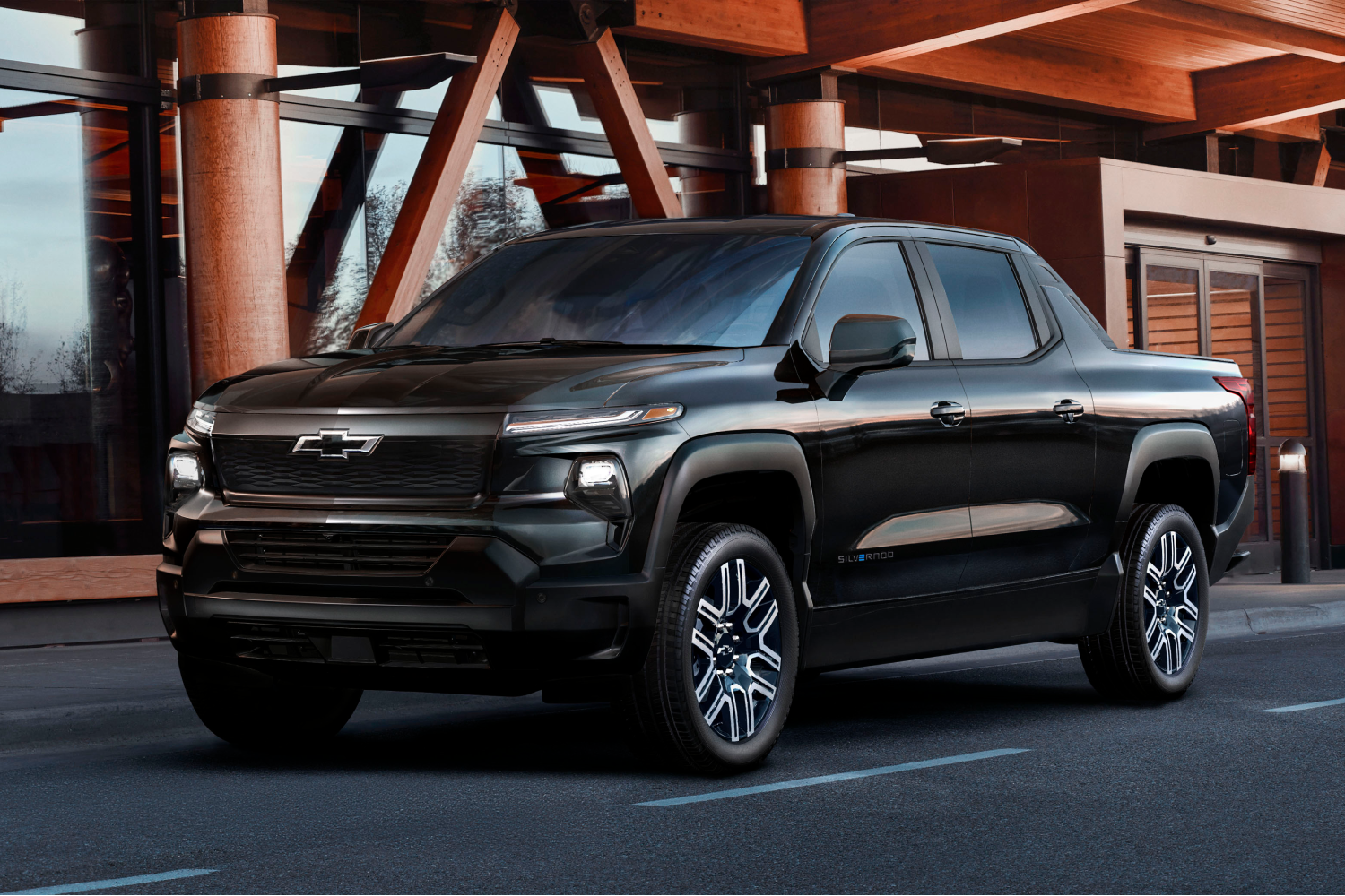 A Black 2024 Chevrolet Silverado EV Pickup Truck is Parked Outside, Showcasing its Sleek Design, Black Grille, and Unique Black and Silver Six-spoke Wheels with the Chevrolet Bowtie Logo in the Center.