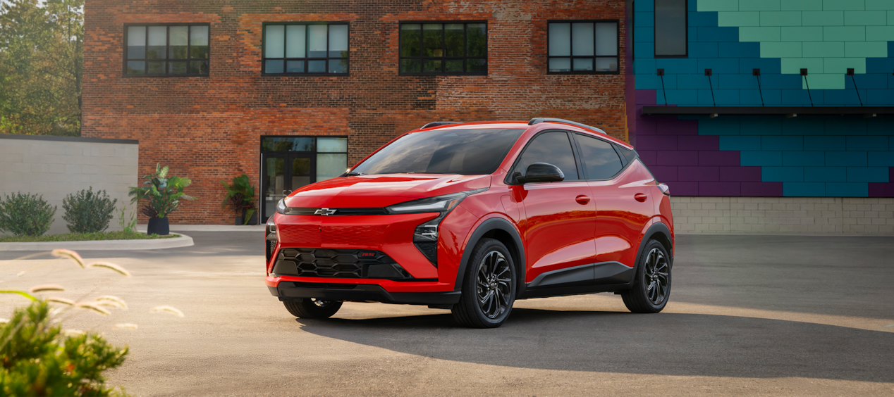 2027 Chevrolet Bolt in Habanero Solid Parked in Front of Brown Wall.