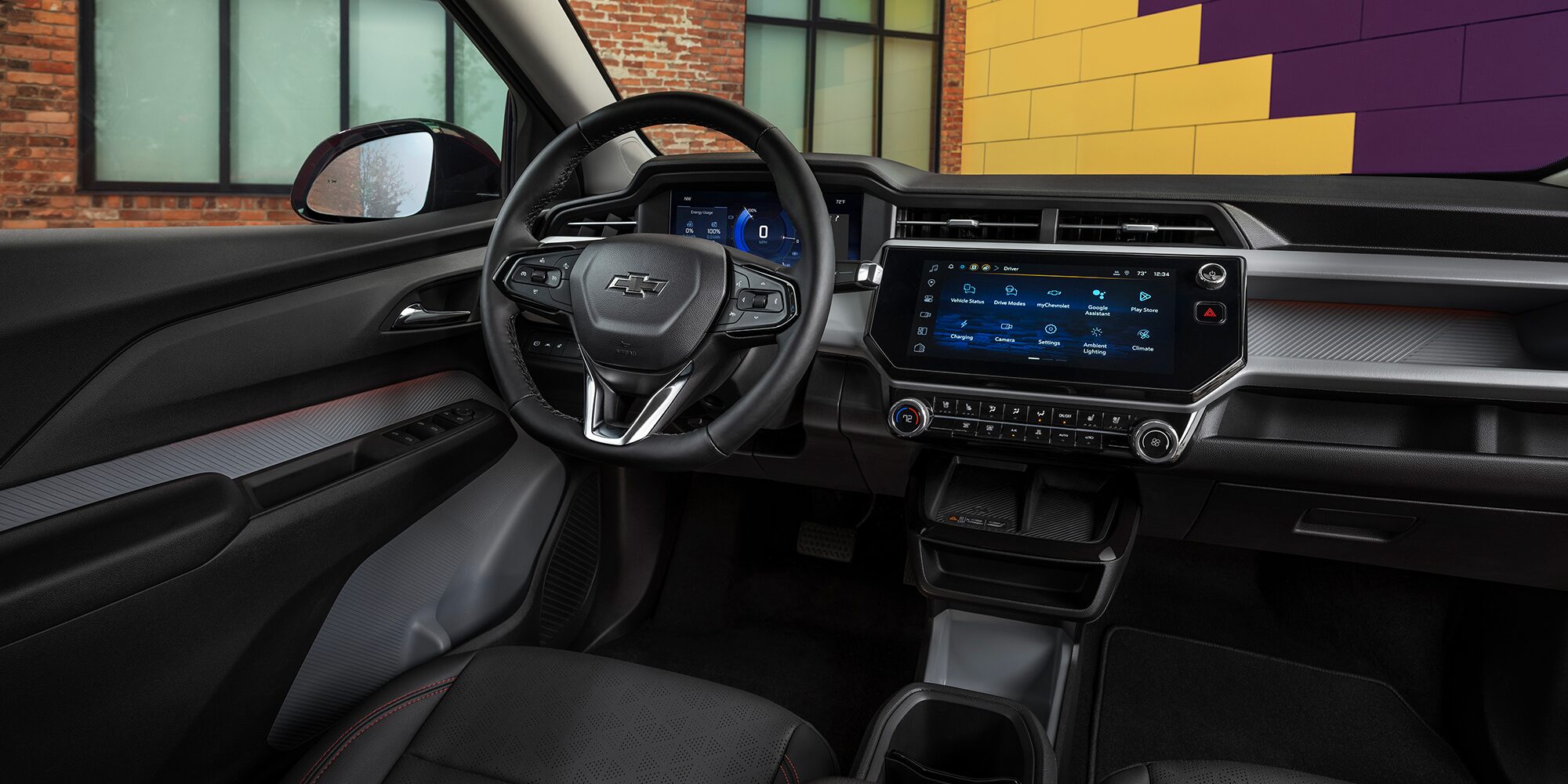 The Interior of a 2027 Chevrolet Bolt, Showing the Driver's Perspective of the Digital Instrument Cluster and a Widescreen Infotainment Screen, with Black Seats and Red Stitching.
