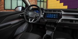 The Interior of a 2027 Chevrolet Bolt, Showing the Driver's Perspective of the Digital Instrument Cluster and a Widescreen Infotainment Screen, with Black Seats and Red Stitching.