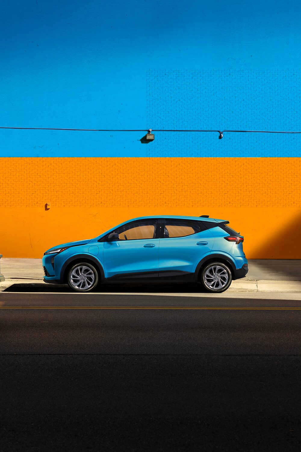 A Marina Blue Metallic 2027 Chevrolet Bolt is Shown in a Side Profile View, with the Text "Bolt Gets Bolder," and Highlights of its New Front and Rear Fascia, 17" Aluminum Wheels, and Gloss Black Outside Mirrors.
