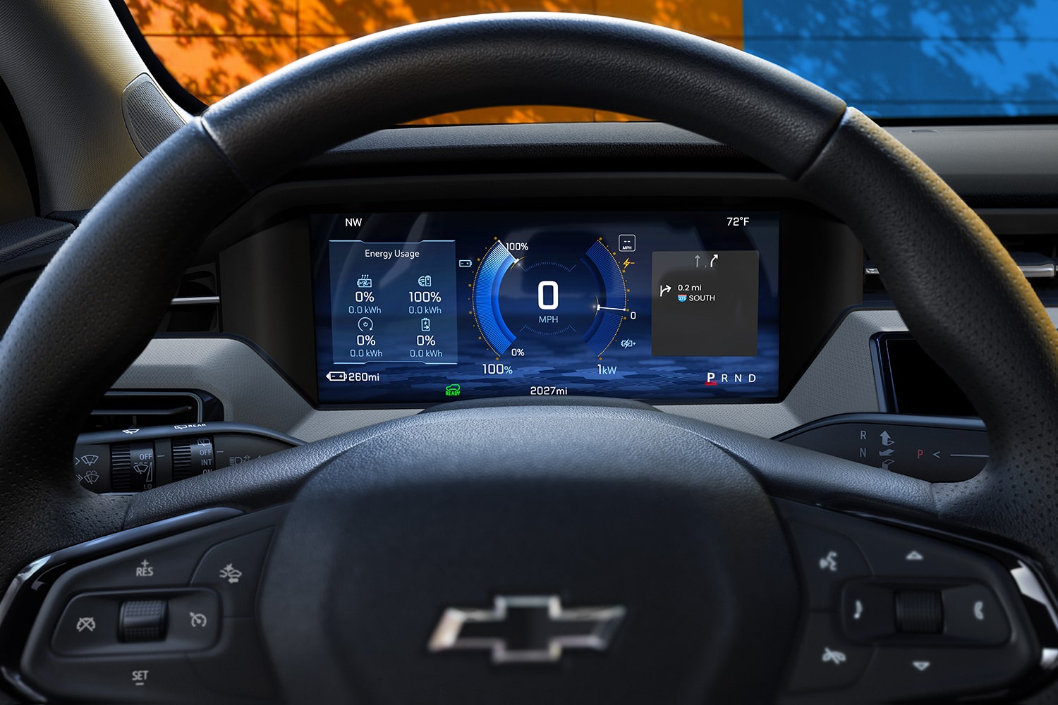 The interior of a 2027 Chevrolet Bolt Shows the Driver's Perspective of the Digital Display Screen behind the Steering Wheel, with a Small Part of the Orange and Blue Exterior Wall through the Windshield.