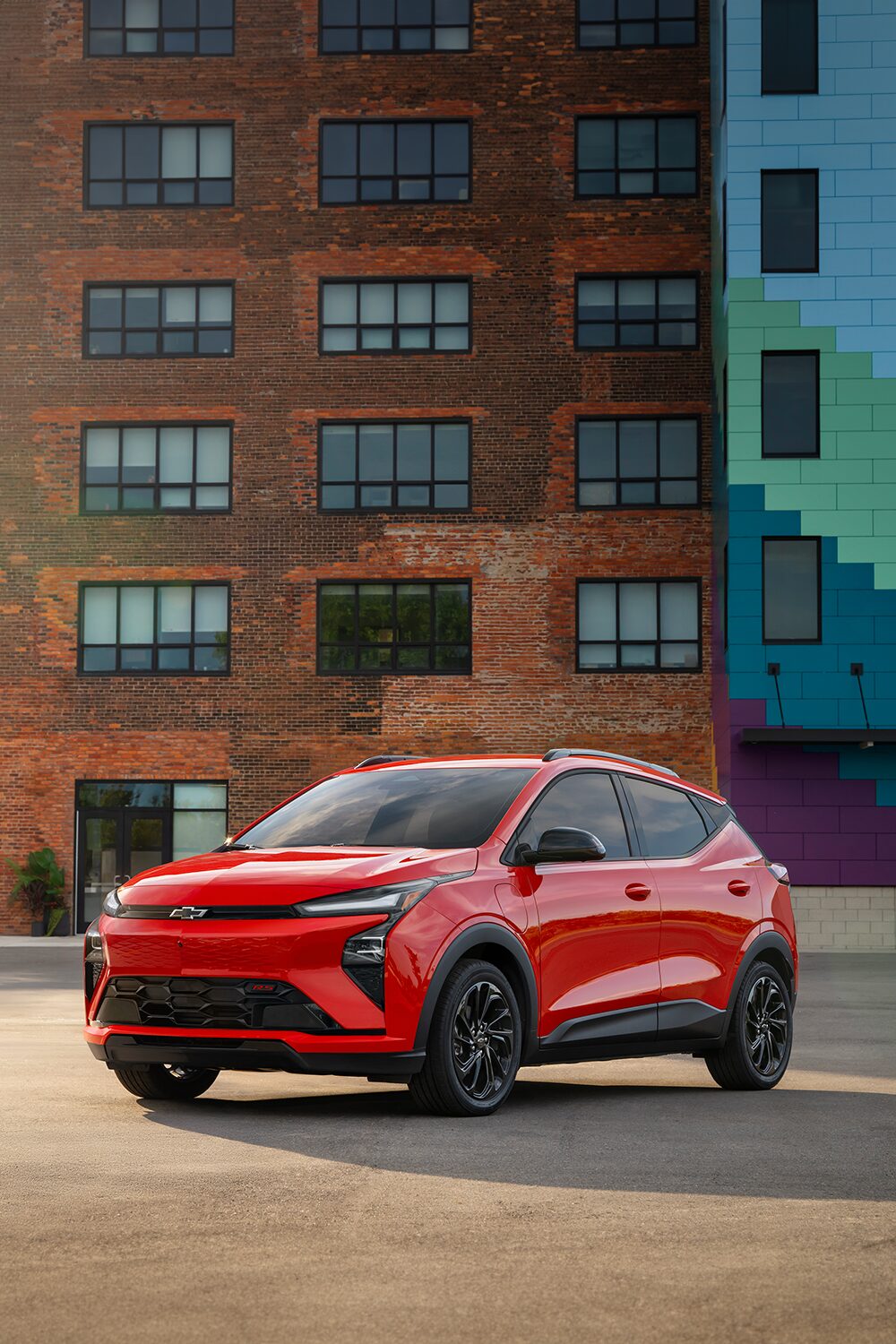 A Habanero 2027 Chevrolet Bolt is Parked in Front of A Brown Brick Building.