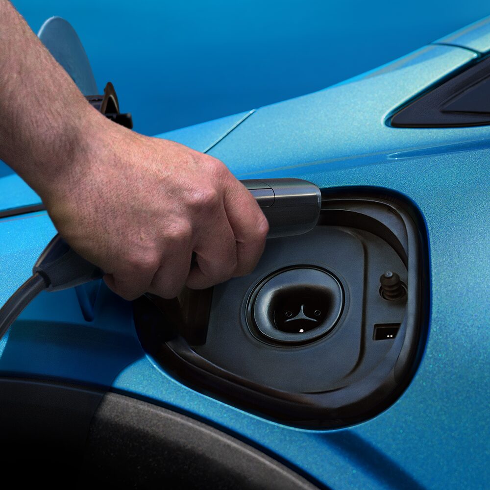 A Hand Plugs a Charging Cable into the Charging Port of a Marina Blue Metallic 2027 Chevrolet Bolt.