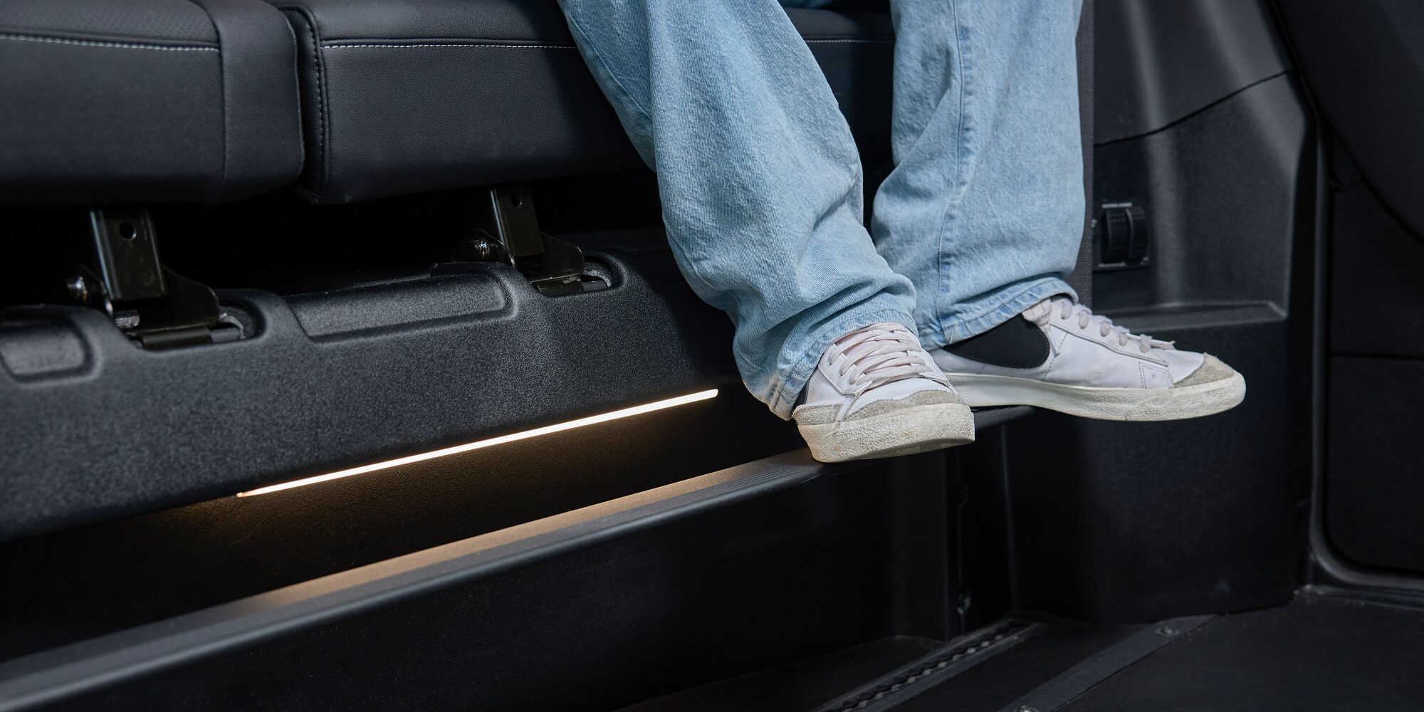The Interior Floor of a Chevy Traverse SUV Showing a Pair of White Sneakers Resting on a Black Footrest Near the Side Panel.