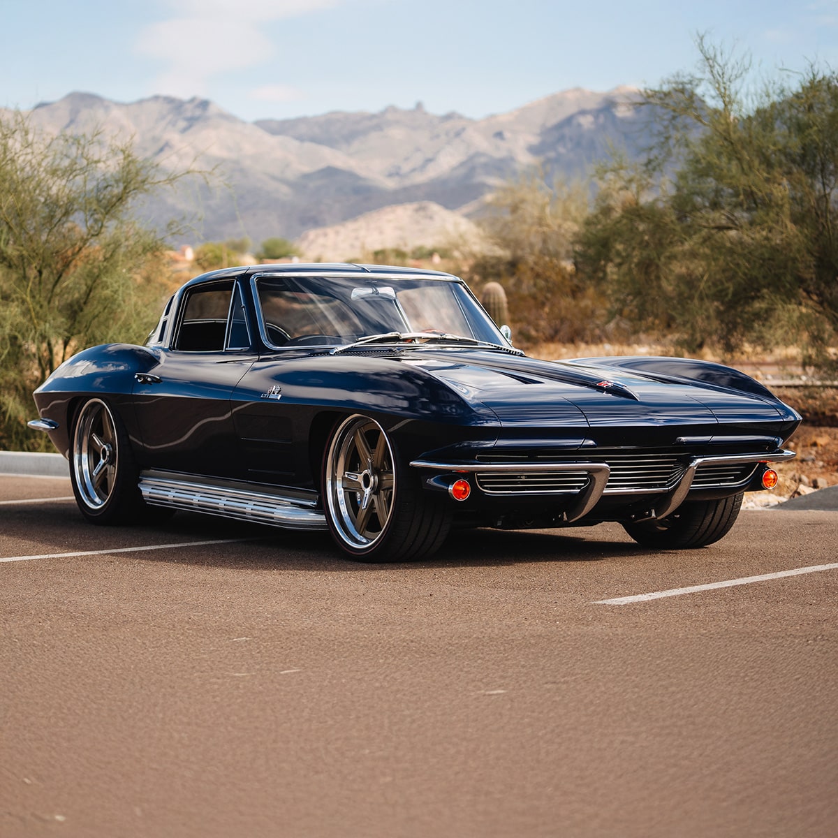 A Classic Blue Chevrolet Corvette Convertible Parked Outdoors on a Sunny Day with Trees in the Background.