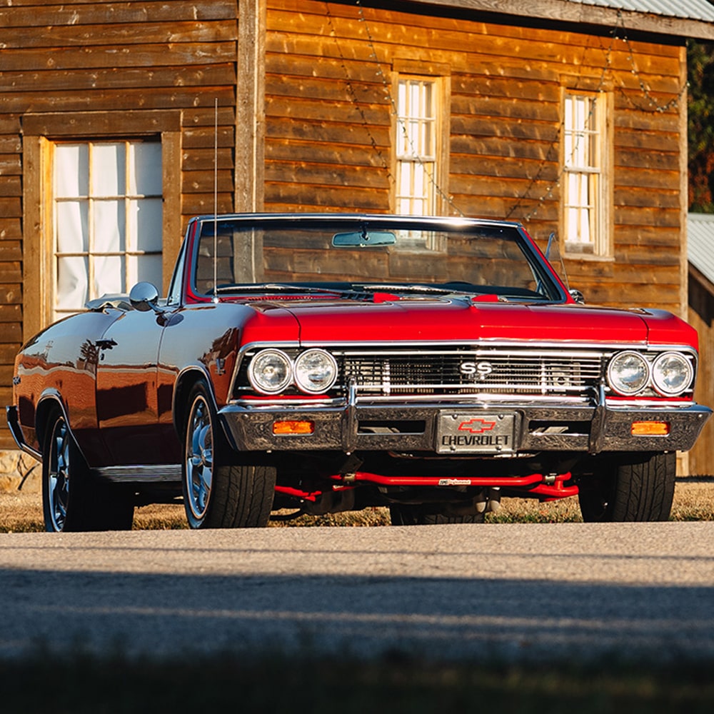 A Red and Black 1966 Chevrolet Chevelle Convertible with Chrome Detailing Parked in Front of a Rustic Wooden Building.
