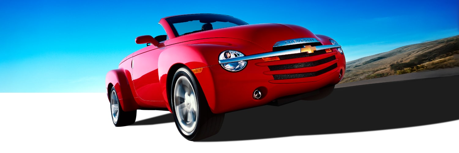 Red Chevrolet Convertible Vehicle Driving on a Road under a Bright Blue Sky with a Front Low-Angle View.