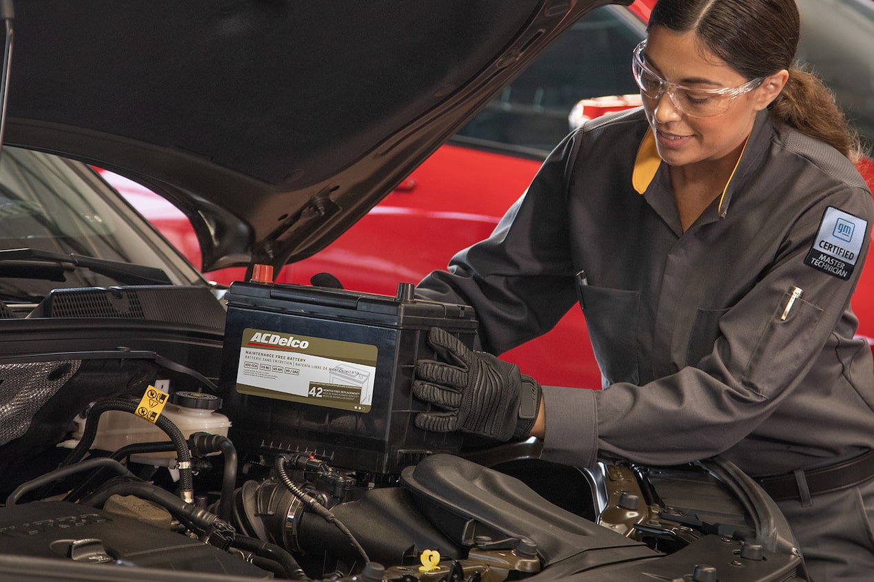 A Mechanic Is Placing a Battery Inside the Front Engine Compartent of a Vehicle