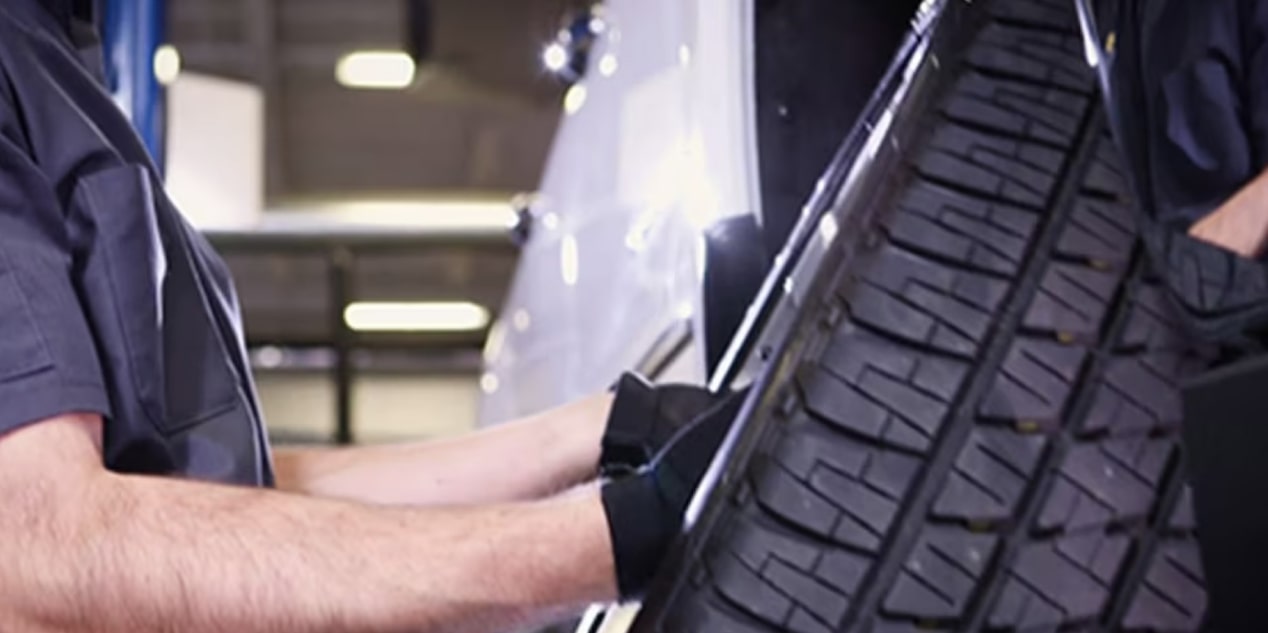 A Mechanic Is Holding a Tire of the Vehicle While Wearing Black Gloves