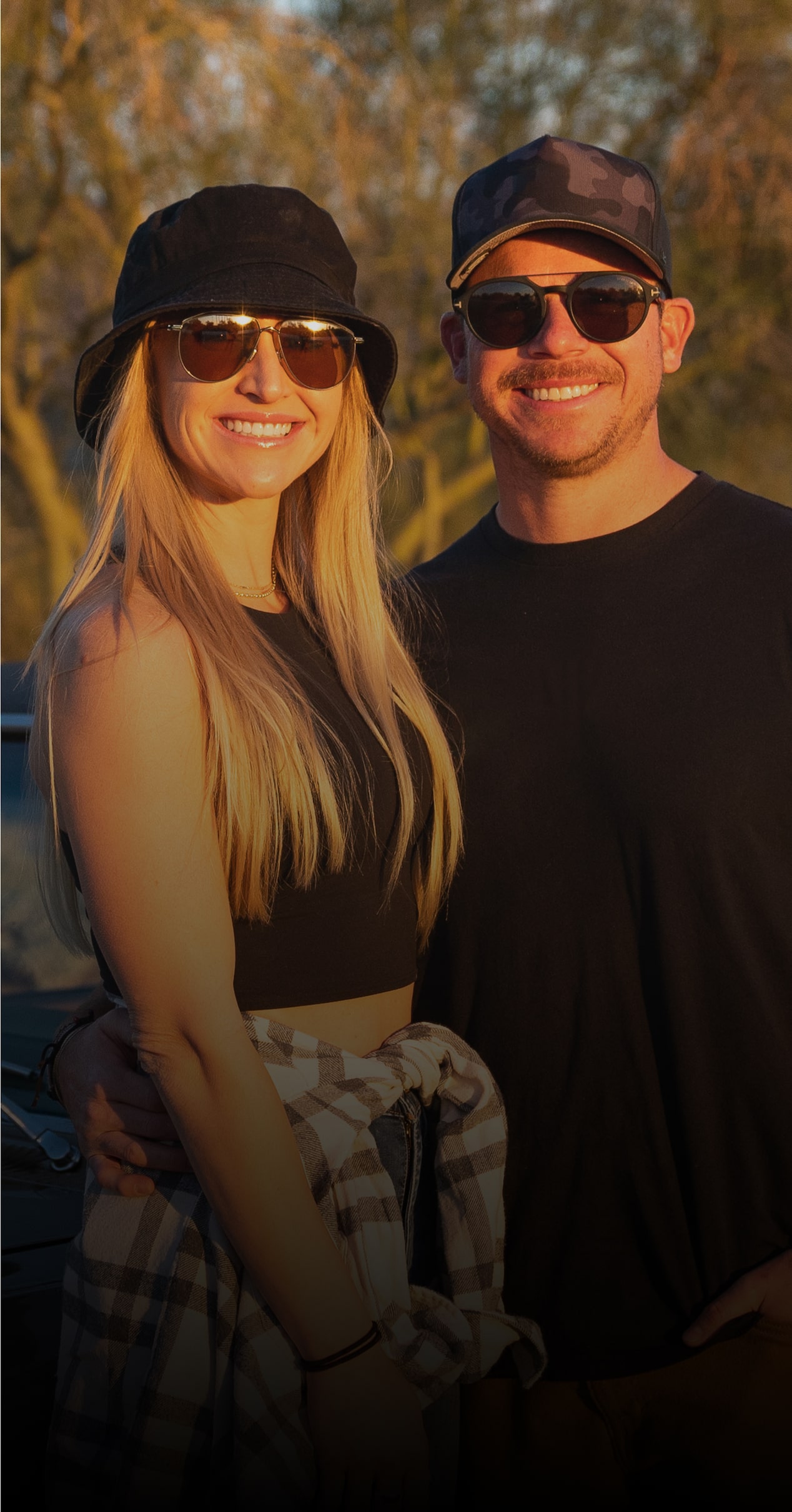 A Man and a Woman Stand Smiling in Front of a Chevy Car During Sunset