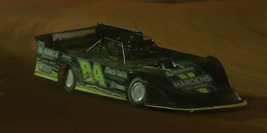 A Black Dirt Track Race Car with the Number 24 on its Side Speeds Around a Curve on a Dirt Track at Night, Kicking up Dust. A Play Button Overlay Suggests this is a Video Still.