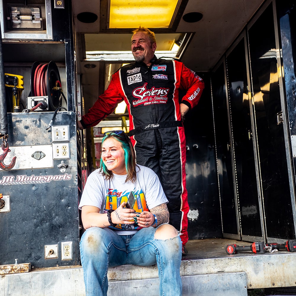 A Race Car Driver Standing Next to His Daughter Who is Sitting in Front of a Shop