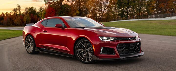 Red Chevrolet Camaro Sports Car Parked on a Racetrack with Autumn Trees and a Sunset Sky in the Back