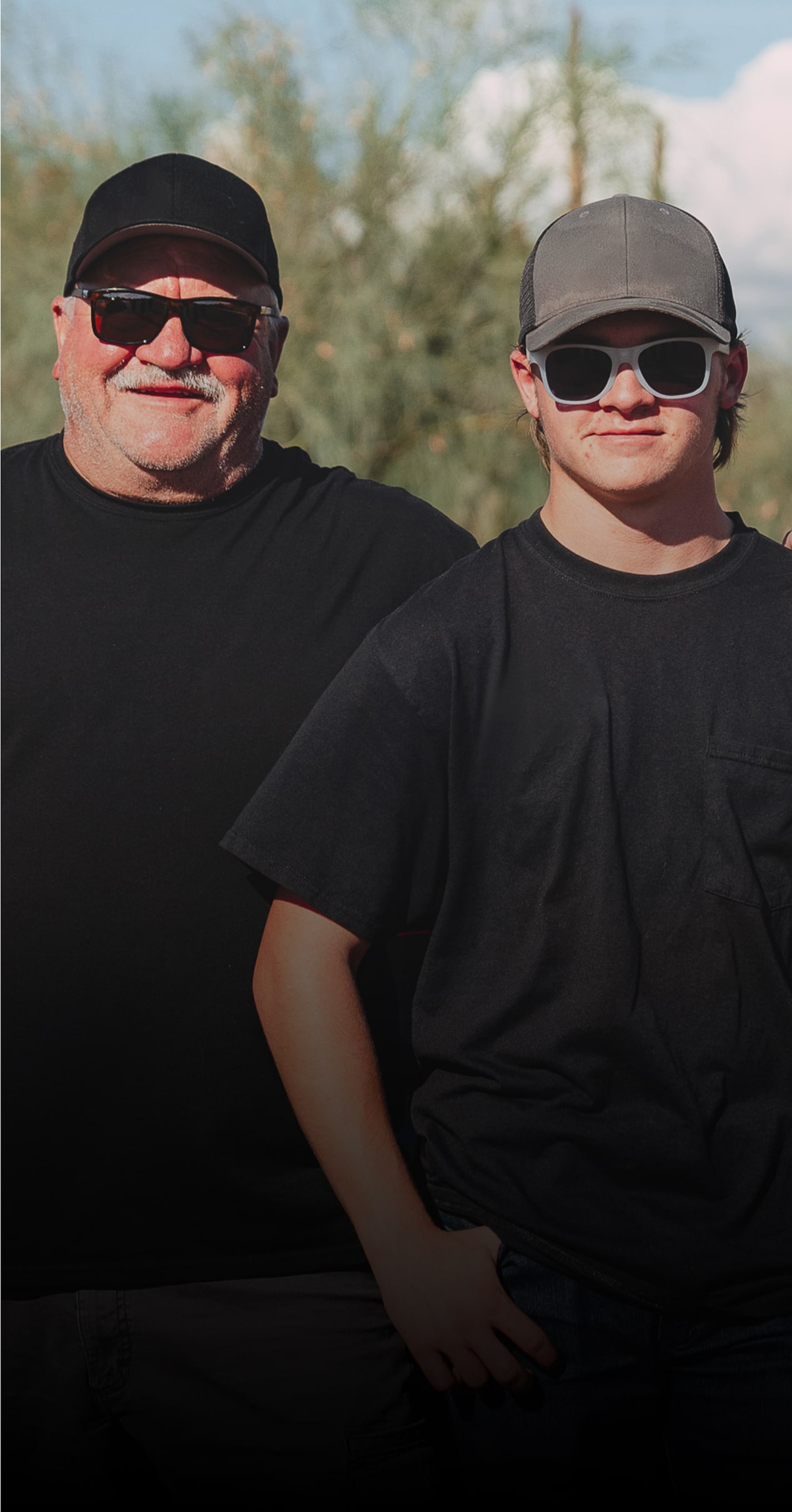 Two Men in Black T-Shirts, Shades, and Ballcaps Stand Outside