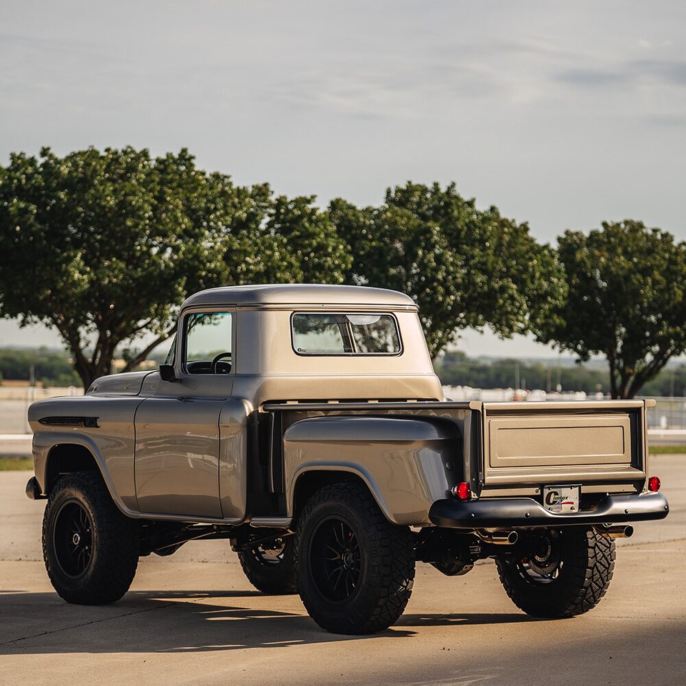 A Rear Side View of a Gold 1958 Chevrolet Apache Pickup Truck Parked in a Parking Lot with Trees in Front of it.
