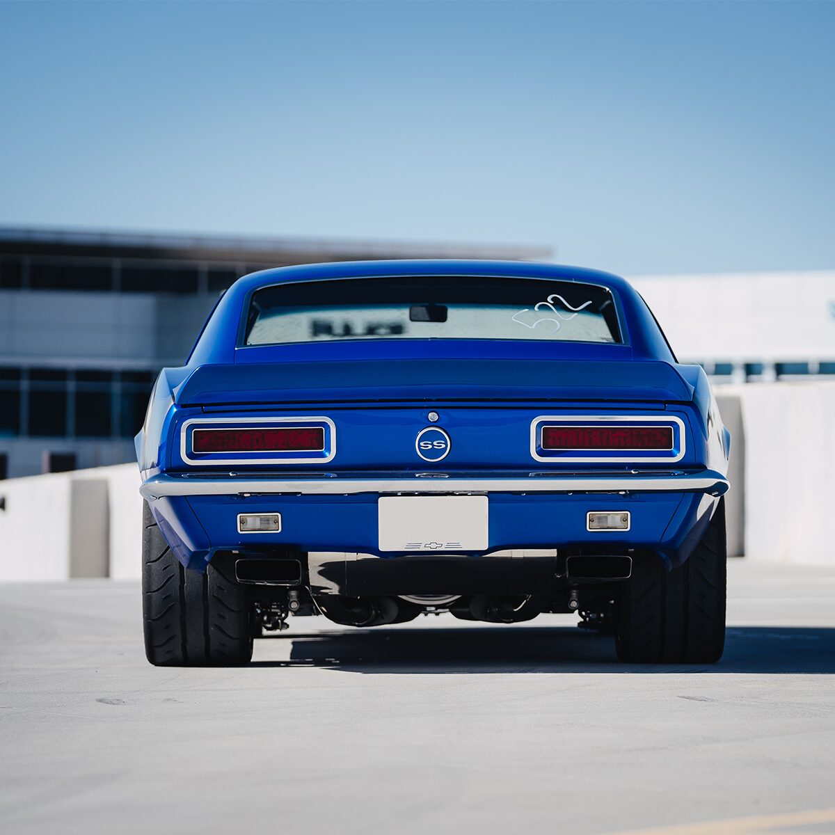 A Rear View of a Blue 1967 Chevrolet Camaro SS Parked in an Open Parking Lot with Building in Front of it.