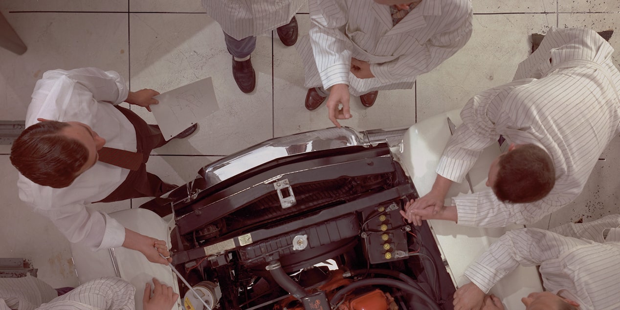 Several Engineers in White Lab Coats Examine a Chevrolet Crate Engine