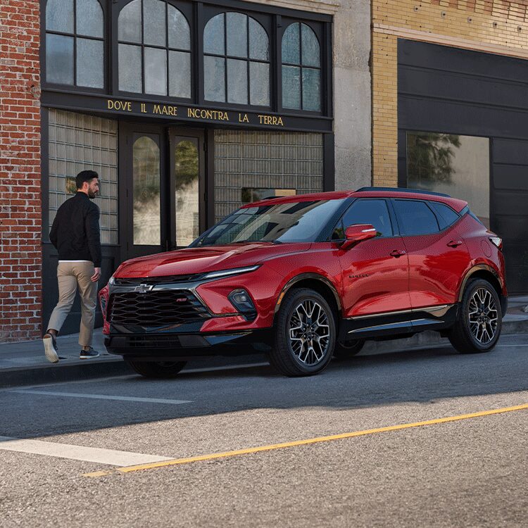 Man Walking Toward His 2026 Red Chevy Blazer Parked at a Shop