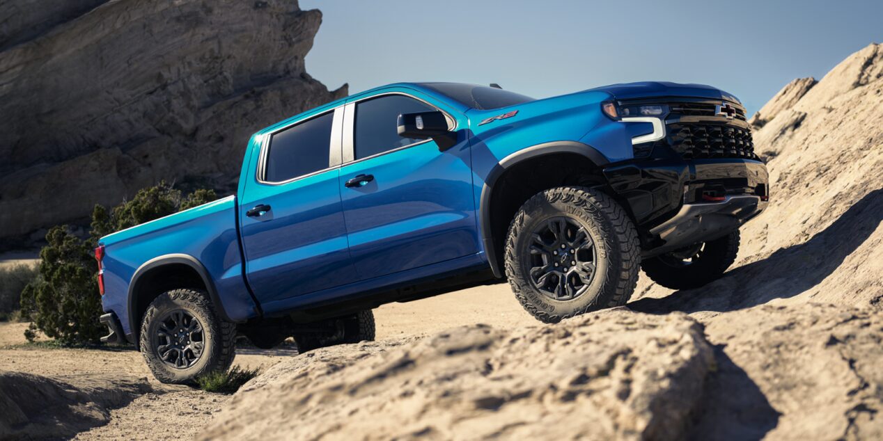 Blue 2026 Chevy Silverado Climbing a Rocky Hill Under Clear Blue Sky
