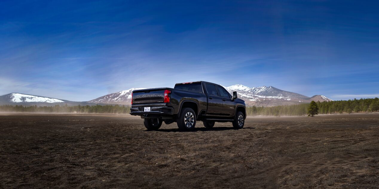 A Black Chevy Silverado LD Driving Across an Open Field with Snow-Capped Mountains in the Distance.