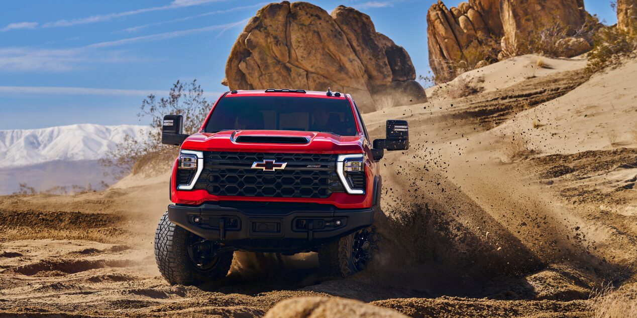 A Red Chevy Silverado LD Driving Through a Rocky Desert Trail with Dust Billowing Behind the Truck.