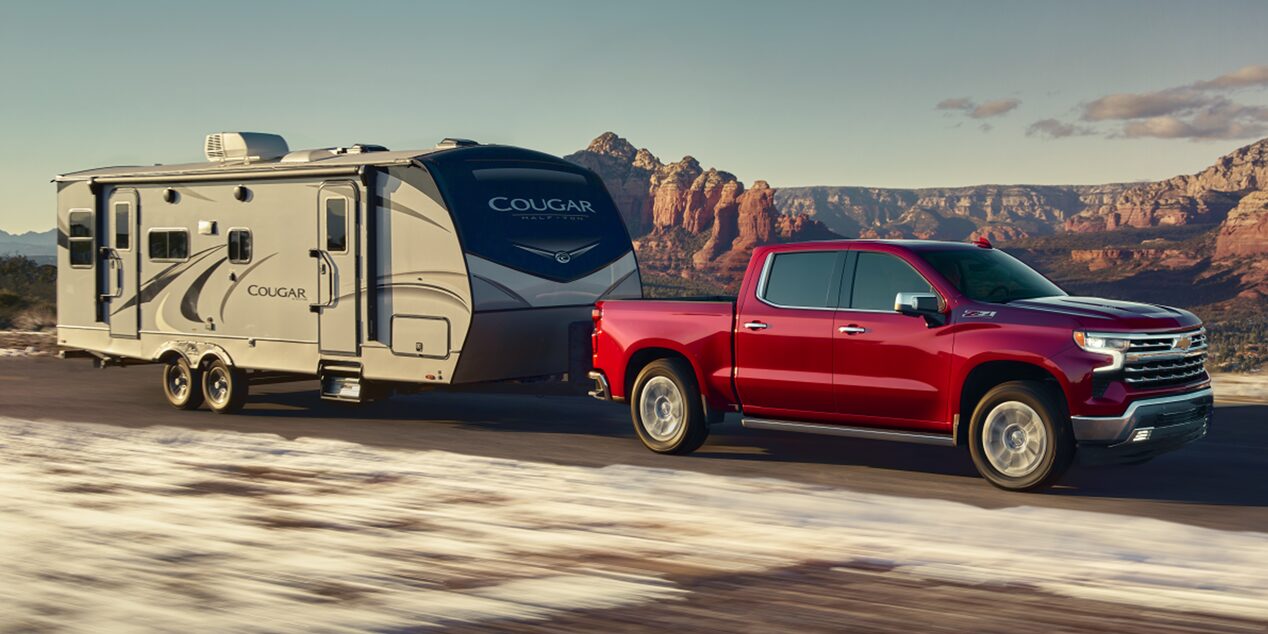 A Red Chevy Silverado 1500 Pickup Truck towing an RV Down a Highway.