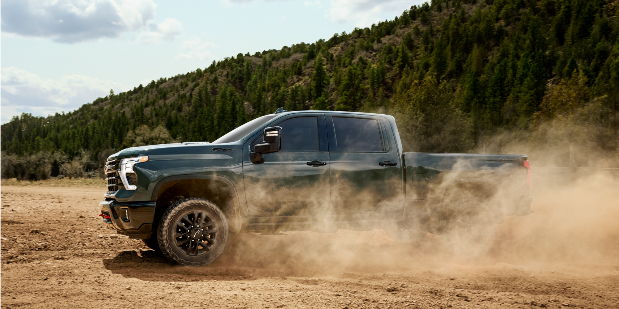 Silverado HD Trail Boss Driving Near a Forest on a Dusty Road