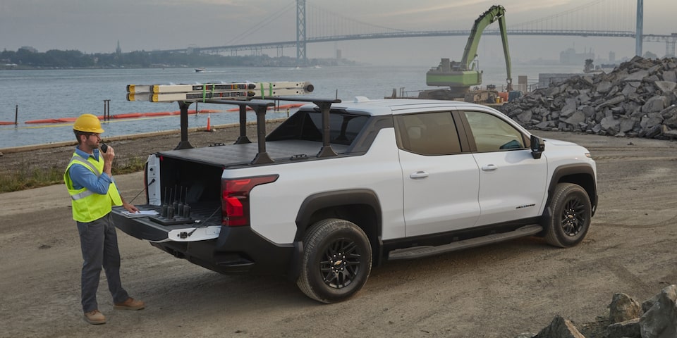 Rear three quarters view of a 2025 white Silverado EV with a man opening the trunk