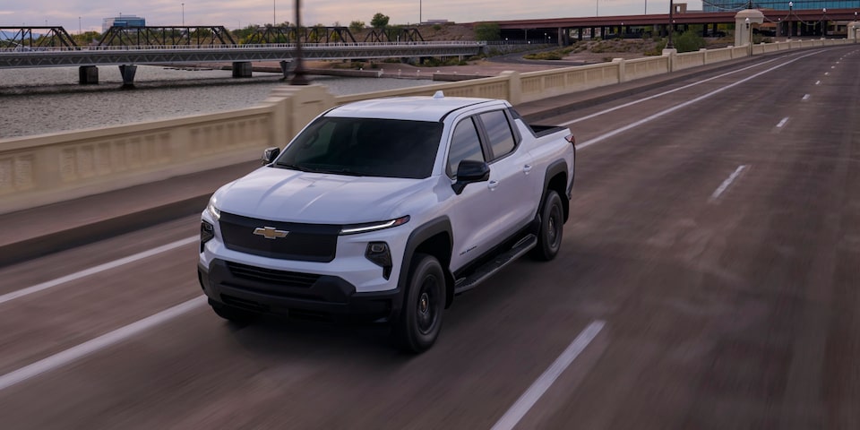 Three quarters view of a Chevy Silverado EV going down a road under the evening sky
