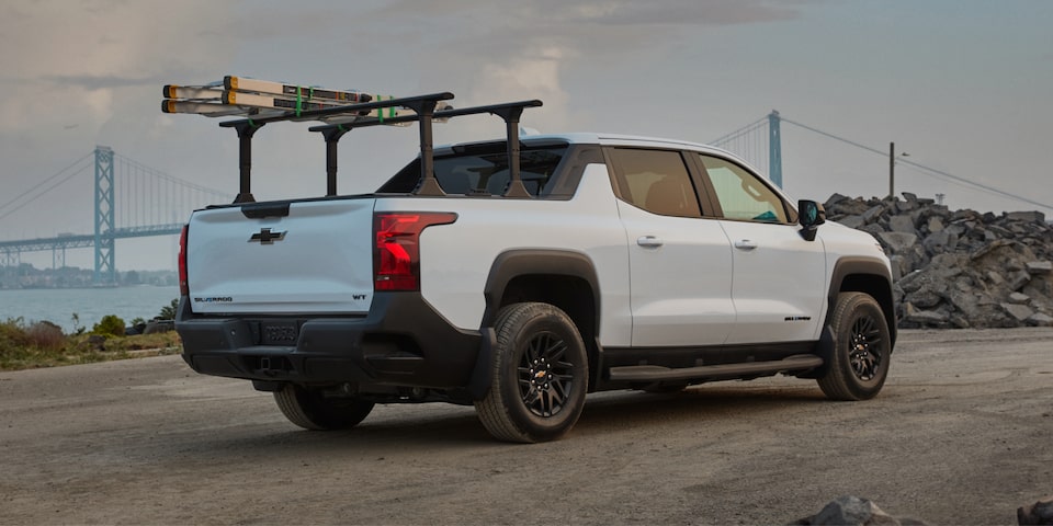 Rear three quarters view of a 2025 white Chevy Silverado EV going down the road in the evening
