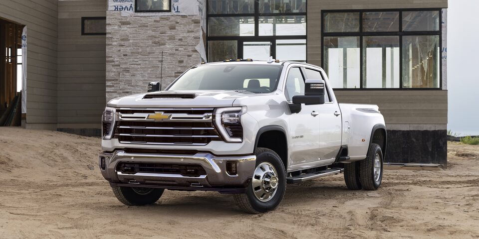 Front Three Quarters View of a White 2025 Chevy Silverado HD Truck in Front of a House