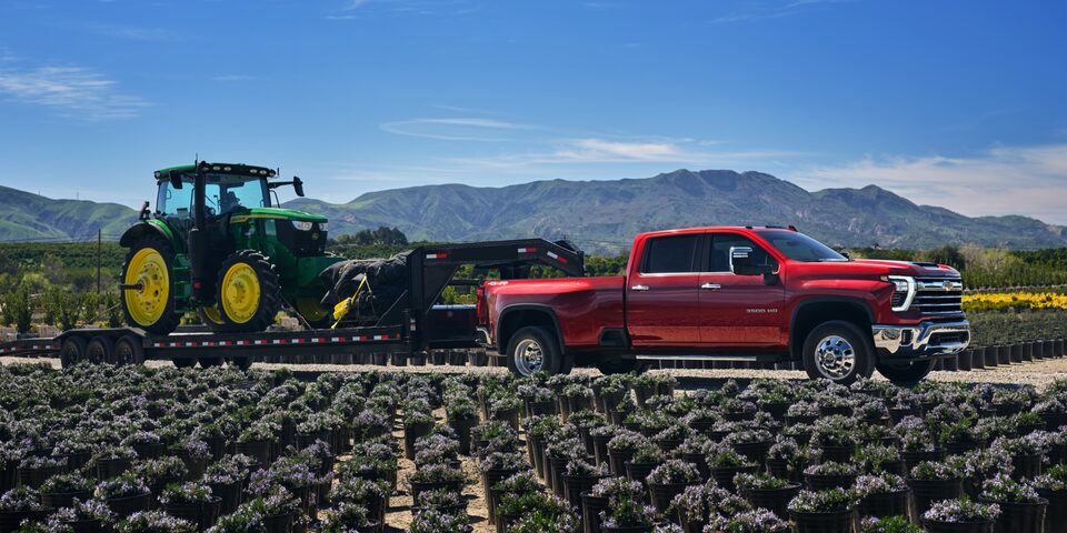 Side View of a Red Chevy Silverado HD Truck Towing a Tractor on a Farm