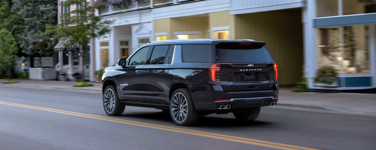 Rear Three-Quarters View of the 2025 Chevrolet Suburban SUV Driving Through Downtown