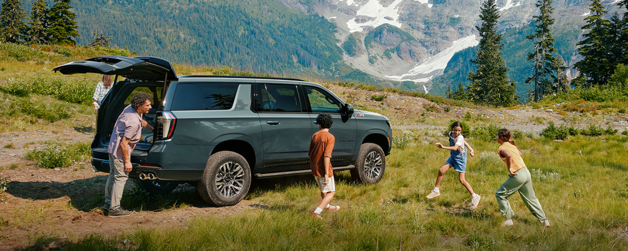 A Family Unloads Their 2025 Chevy Suburban While Parked in a Field Near Mountains