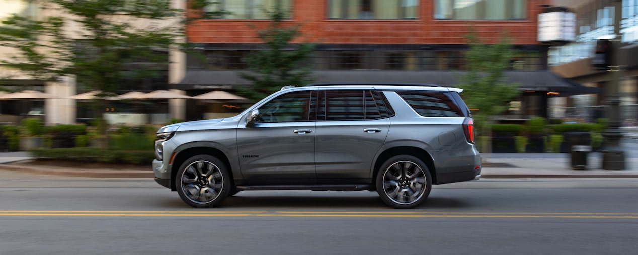 Side View of the 2025 Chevrolet Tahoe SUV Driving on a Road Lined with Businesses