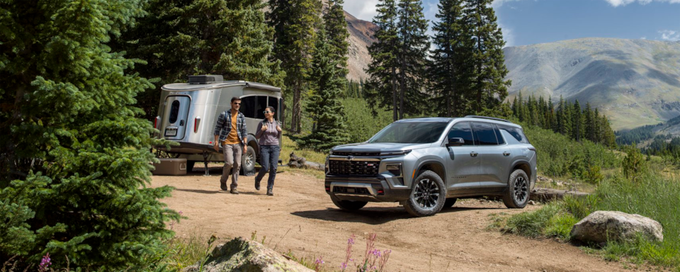 Three Quarters View of a Silver Chevy Traverse with a Man and a Woman Walking in Front of a Trailer