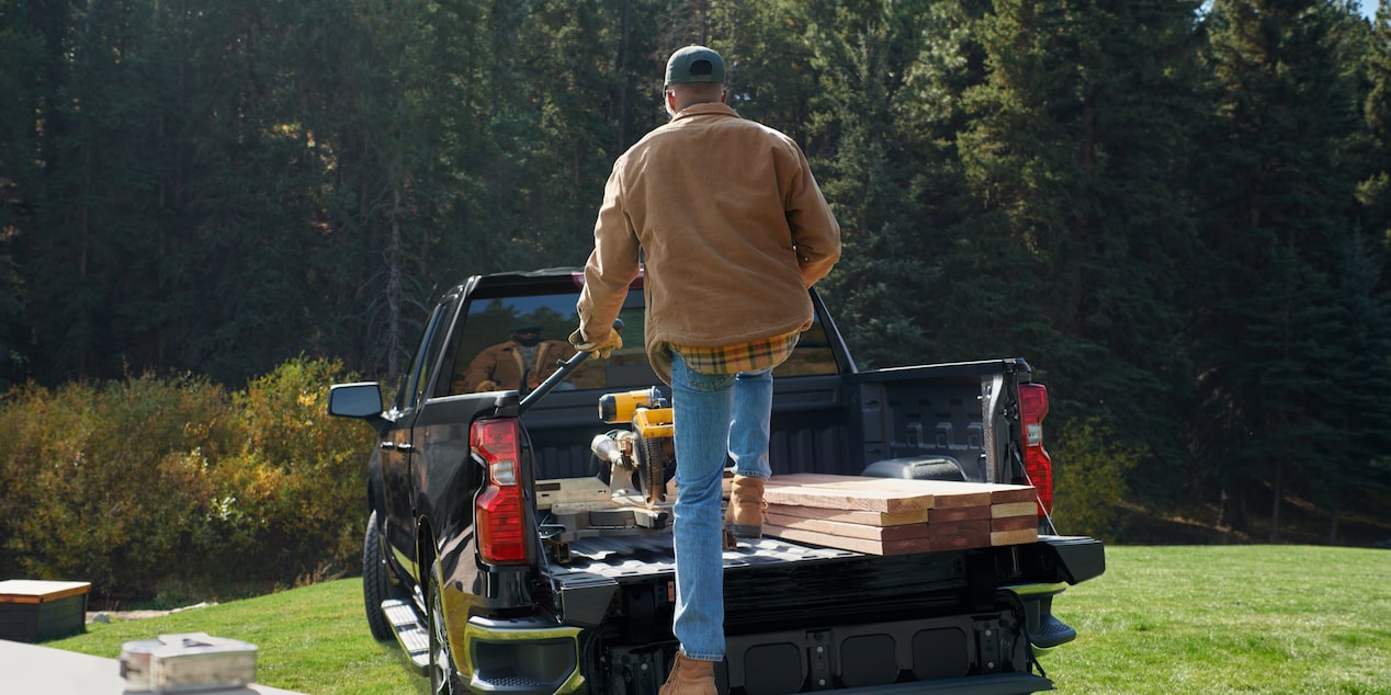 A Man Putting Wood and Other Equipment on the Trunk of a Chevy Silverado Pickup Truck