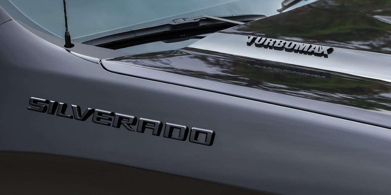 Three Quarters View of a 2025 Black Chevy Silverado Pulling a Trailer with a Red Lawn Mower