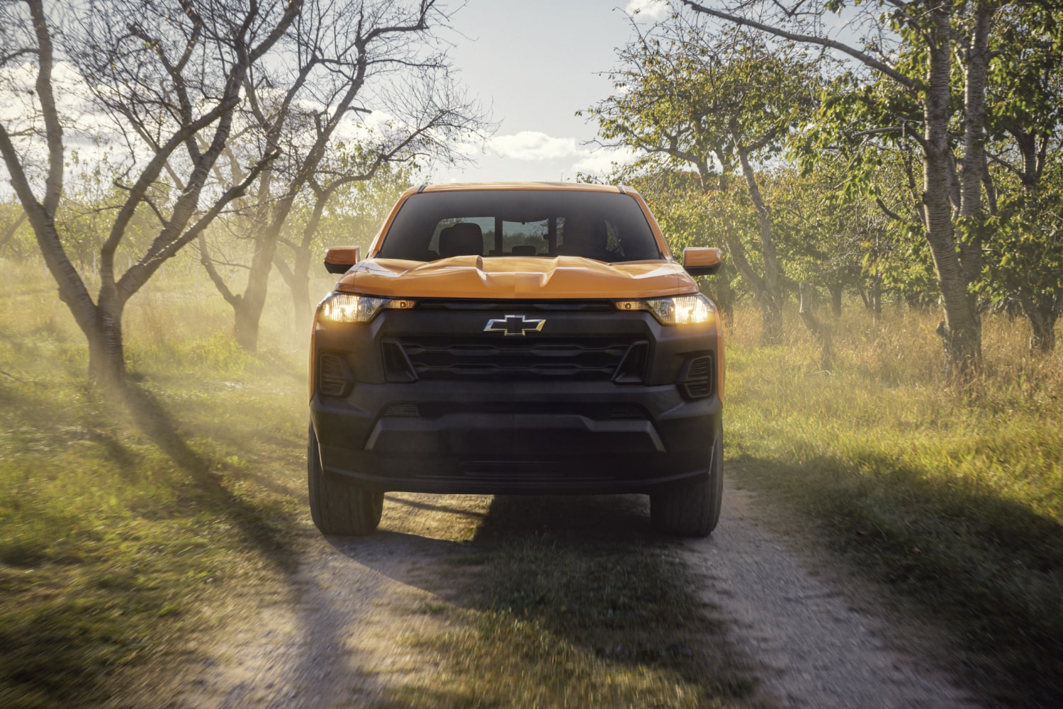 Front View of a Yellow 2026 Chevy Colorado Pickup Truck Going Down a Road with Trees on Both Sides