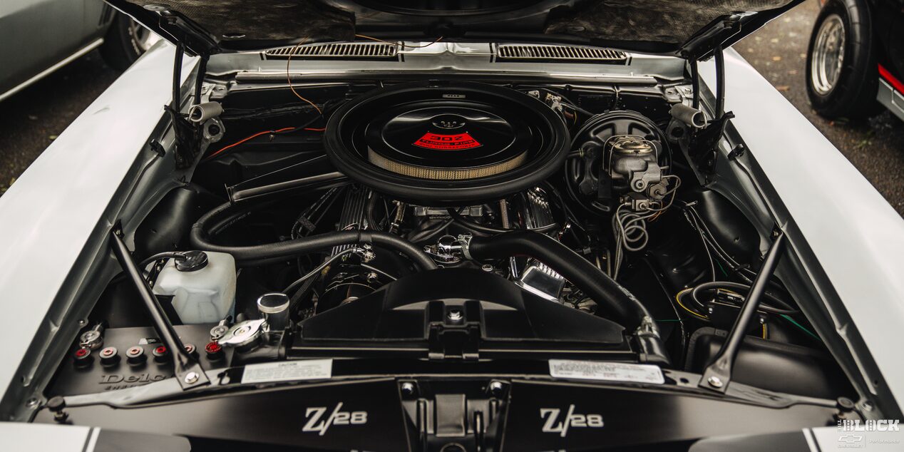 Front View of a White Chevy Car Engine with a Cylindrical Air Filter in the Middle